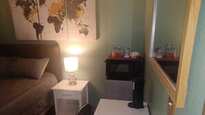 Ett hotellrum med en säng, ett skrivbord med en lampa, ett litet kylskåp och en världskarta på väggen.