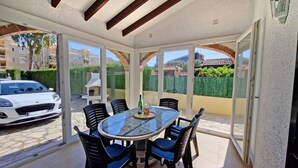 A sunlit patio with a glass table and chairs, a car parked outside, and a view of a residential area. - La Gallega - Denia, Costa Blanca (Denia)