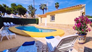 A swimming pool with lounge chairs, a potted plant, and a building with a tiled roof. - La Gallega - Denia, Costa Blanca (Denia)