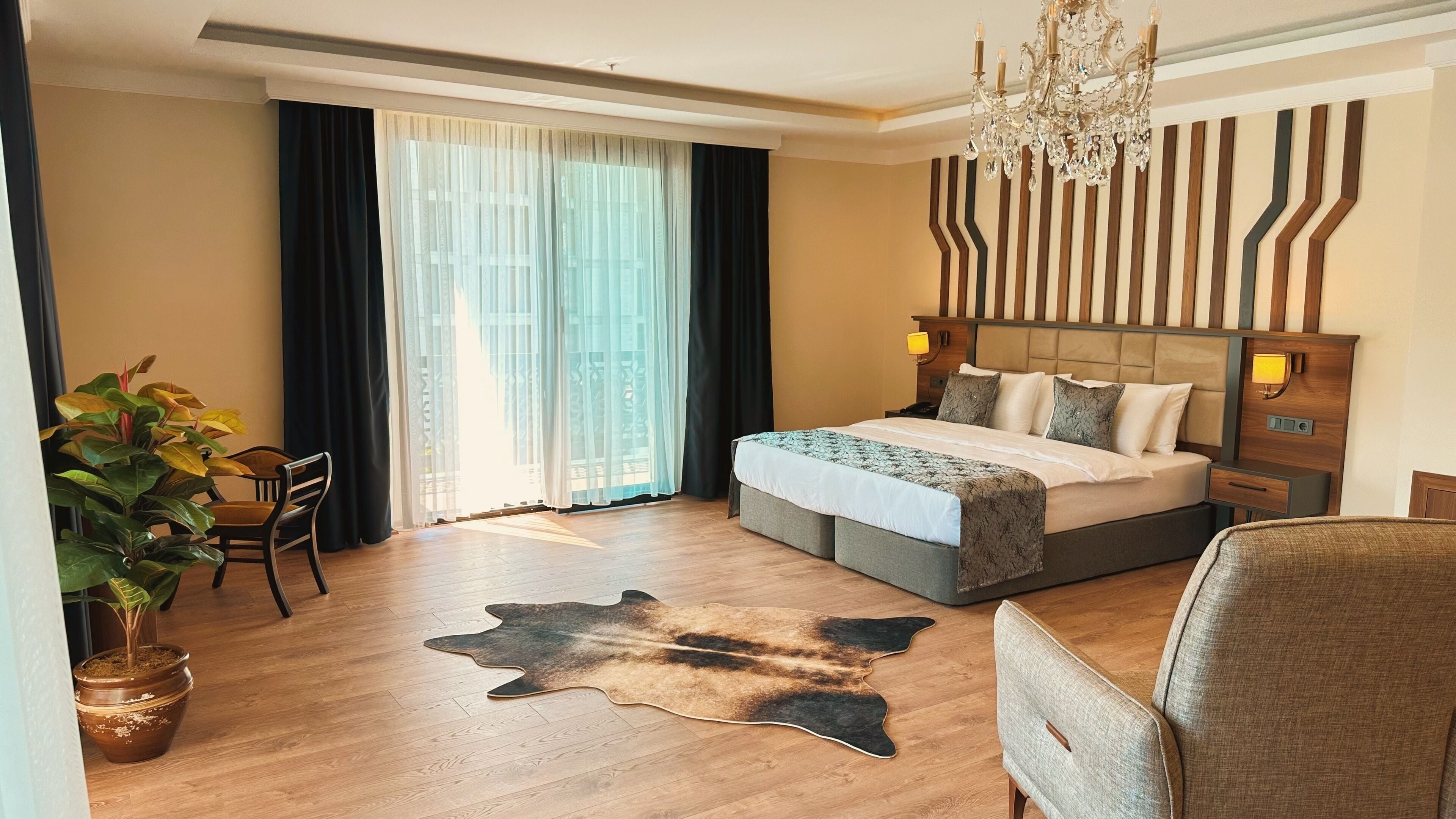Una habitación de hotel con una cama grande, un candelabro, un escritorio con lámpara y una planta en maceta.