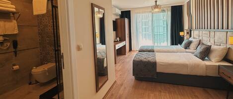 Habitación de hotel con suelo de madera, una cama grande con cabecero, una mesita de noche, un espejo, un armario y un baño con inodoro y zona de ducha.