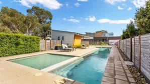 Una piscina amb terrassa solària, una casa moderna al fons i una tanca de fusta.