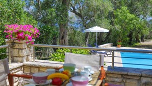A terrace with a pool, stone balustrade, and a table set with cups and fruits.