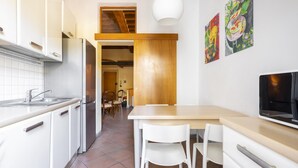 Una cocina moderna con armarios blancos, un refrigerador de acero inoxidable, una mesa de comedor de madera con dos sillas blancas y un televisor Samsung.