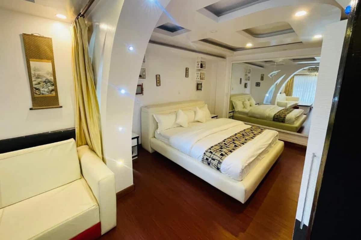 A modern bedroom with a large bed, a sofa, and a mirror reflecting the room.