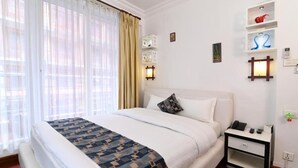 Habitación de hotel con una cama grande, una mesita de noche con teléfono y lámpara, y un estante en la pared con objetos decorativos.