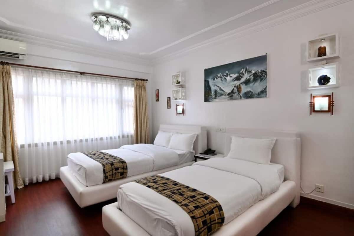 A hotel room with two beds, a chandelier, a painting, and a window with curtains.