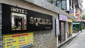 Un hotel llamado 'SQUARE' con un cartel que anuncia servicios como senderismo, boletos de avión, pasajes de autobús y alquiler de coches.