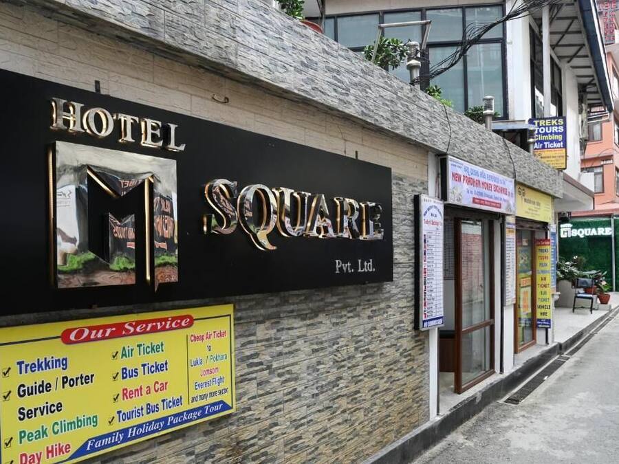 Un hotel llamado 'SQUARE' con un cartel que anuncia servicios como senderismo, boletos de avión, pasajes de autobús y alquiler de coches.