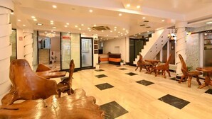 Un vestíbulo de hotel con mostrador de recepción, sillas de madera, una escalera y una zona de recepción.