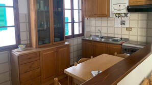 Een keuken met houten kastjes, een eettafel en een raam met groene luiken.
