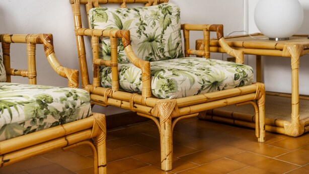 Een kamer met twee rieten stoelen met bloemenmotieven, een kleine tafel met een witte, bolvormige lamp en een betegelde vloer.
