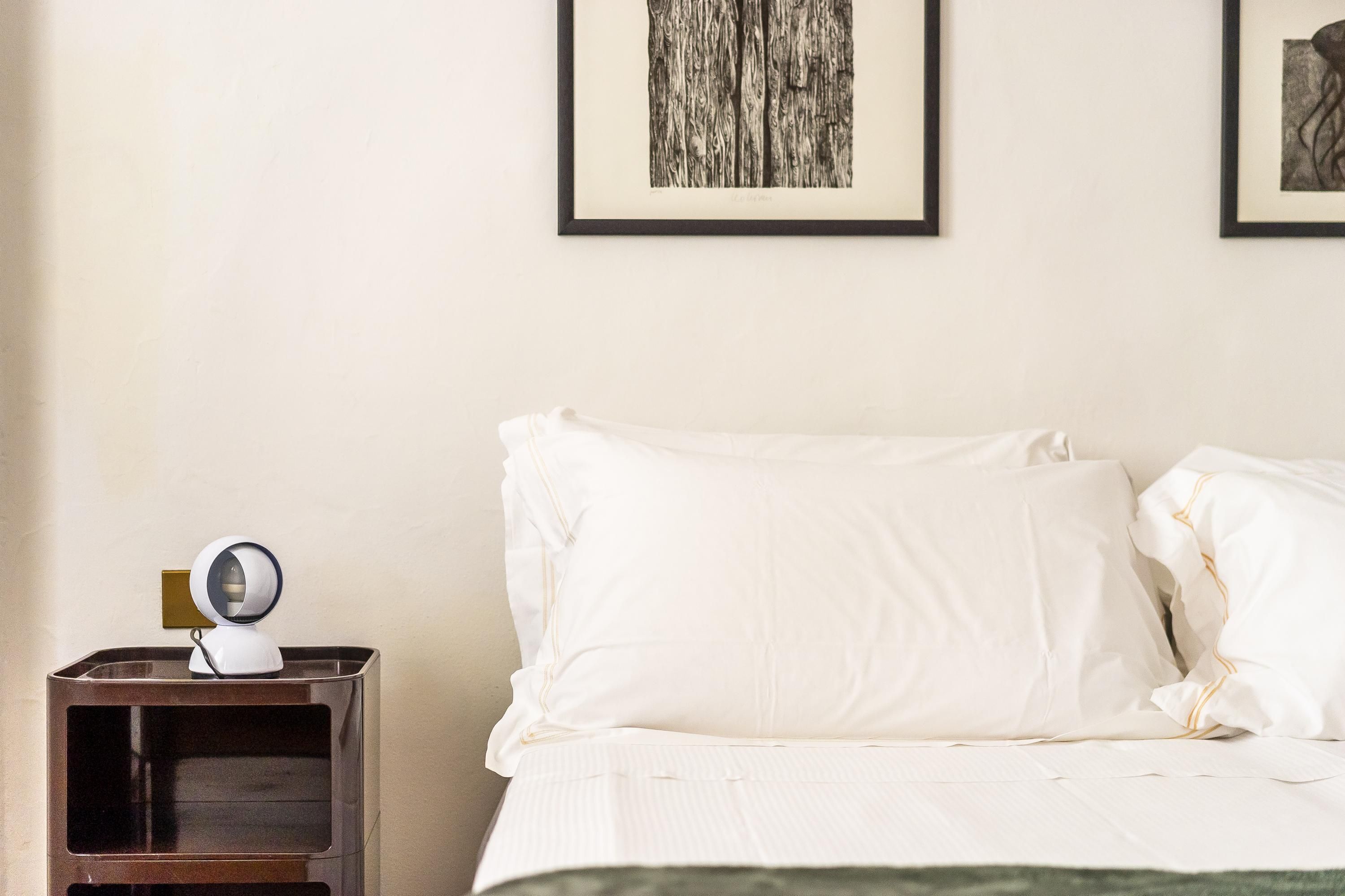 A neatly made bed with white linens and a small bedside table with a lamp.