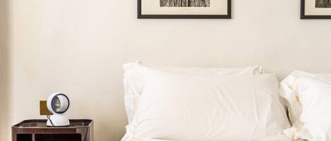 A neatly made bed with white linens and a small bedside table with a lamp.