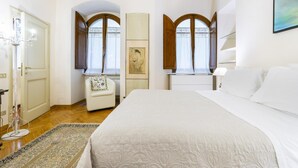 A bedroom with a large bed, a chair, a desk, and two windows with curtains.