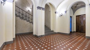 A spacious hallway with a patterned tile floor, a staircase with ornate railings, and a wooden door.