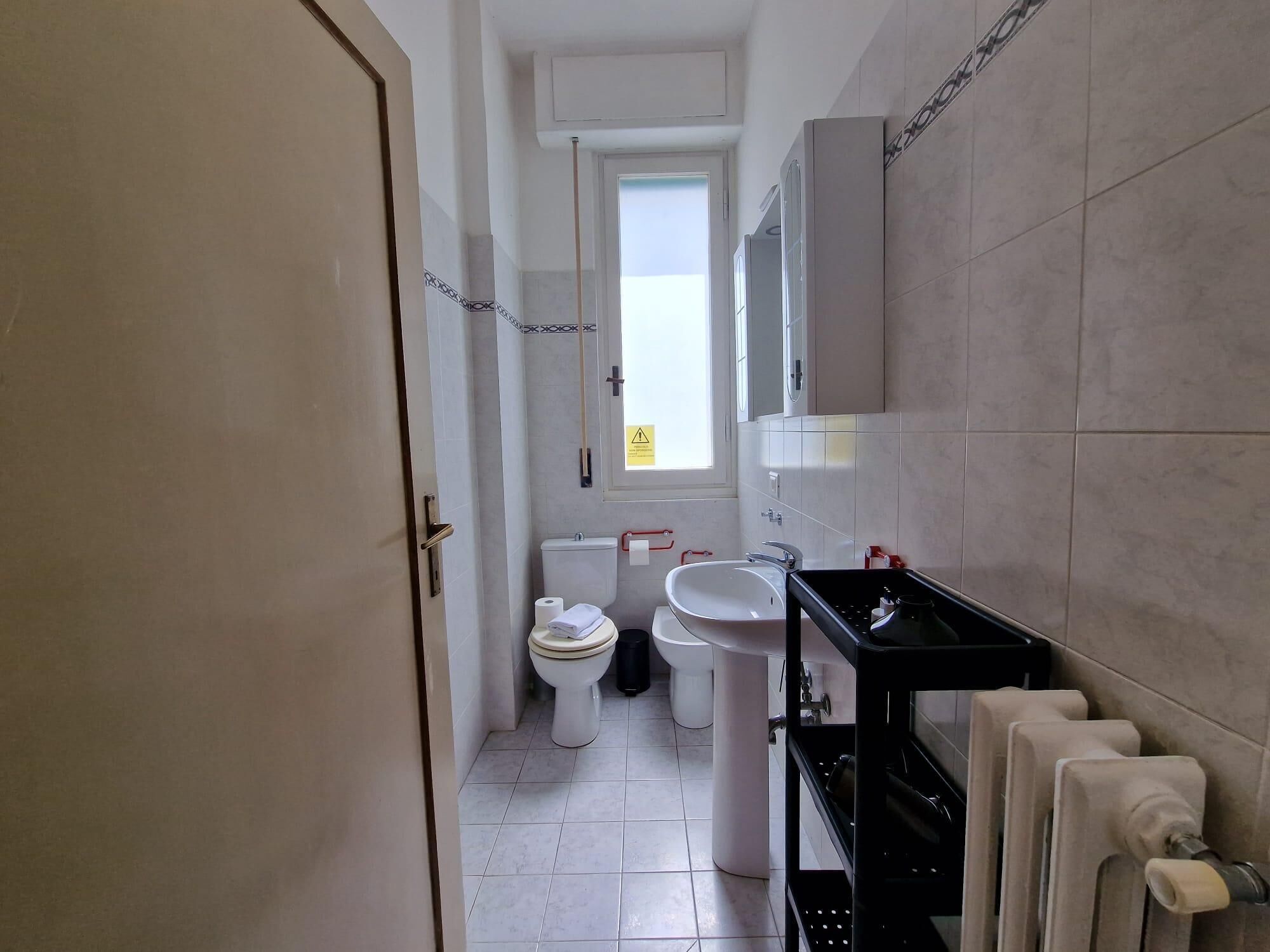 A bathroom with a toilet, bidet, sink, and a towel rack.
