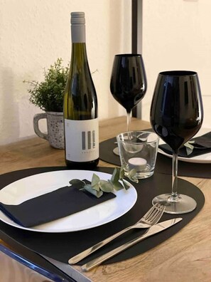 A dining table with a bottle of wine, two wine glasses, a plate, cutlery, and a napkin. - Studio apartment moor-home (Ganderkesee)