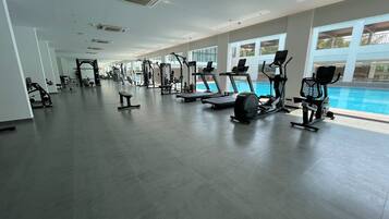 A spacious gym with various exercise equipment, large windows, and a pool area.