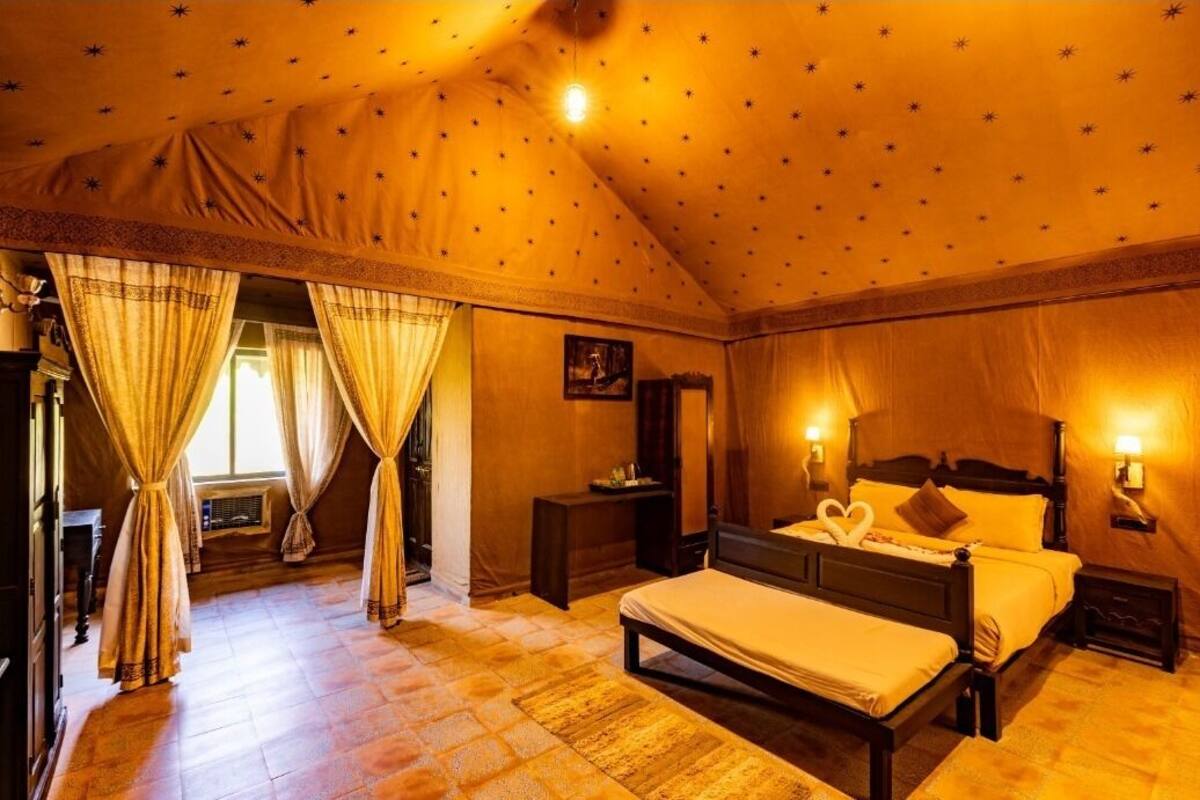 A cozy bedroom with a large bed, a nightstand, a dresser, and a window with curtains.