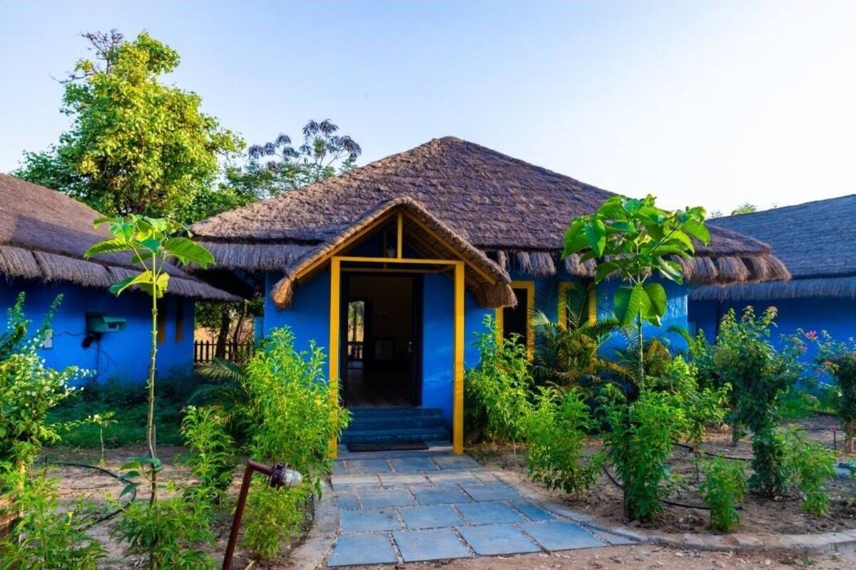 A traditional house with a thatched roof, a blue exterior, and a wooden front door.