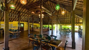 Un restaurante de planta abierta con mesas y sillas de madera, faroles colgantes y un tejado de paja.