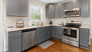 A modern kitchen with grey cabinets, stainless steel appliances, a dishwasher, and a window with blinds.