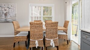 A dining area with a wooden table and wicker chairs, a chandelier, and a window with blinds.