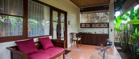 A room with a wooden sofa, a dining table with chairs, and a kitchen area.