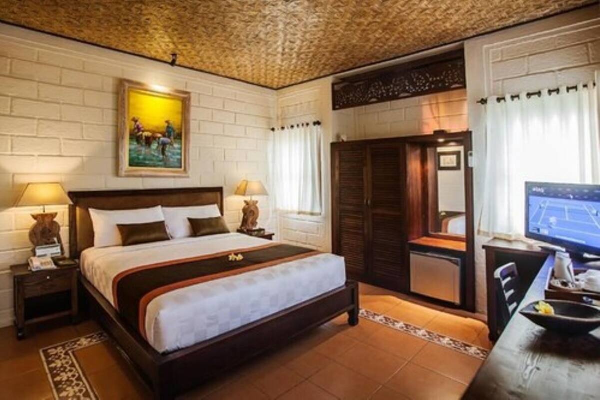Habitación de hotel con una cama grande, dos mesitas de noche con lámparas, un escritorio con ordenador y un armario.