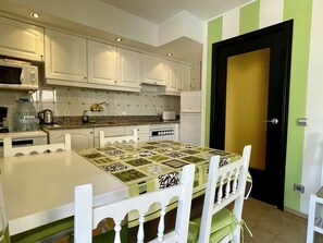 Une cuisine avec des meubles blancs, un four à micro-ondes, un réfrigérateur et une table à manger avec des chaises.