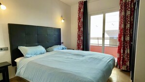 Ein Hotelzimmer mit einem großen Bett, einem Nachttisch, einer Wandleuchte und einem Fenster mit Vorhängen.