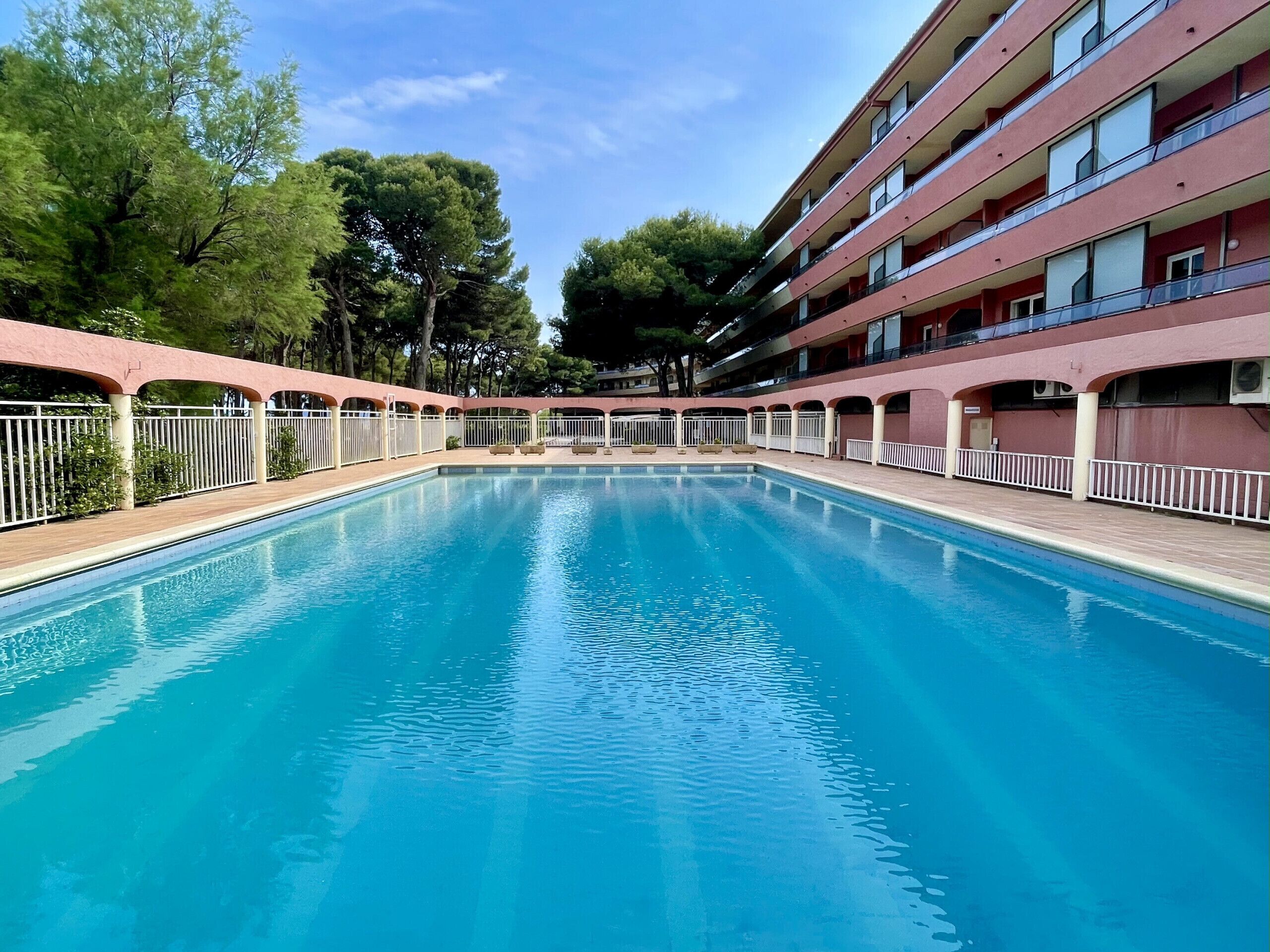 Una piscina con muelle de madera, rodeada por un edificio rosa con balcones.