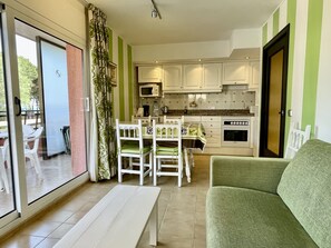 A modern kitchen with white cabinets, a dining table with chairs, and a green sofa. - SALLES BEACH 9 (Estartit)