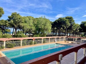 A swimming pool with a tiled deck, surrounded by a metal fence and trees. - SALLES BEACH 9 (Estartit)