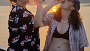 Deux personnes boivent dans des canettes, avec un coucher de soleil et des montagnes en arrière-plan.