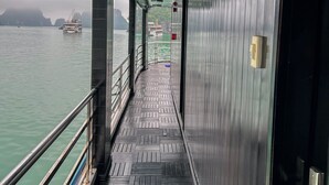 Un couloir donnant sur l’eau et les bateaux, avec des garde-corps en métal et un sol à motifs.