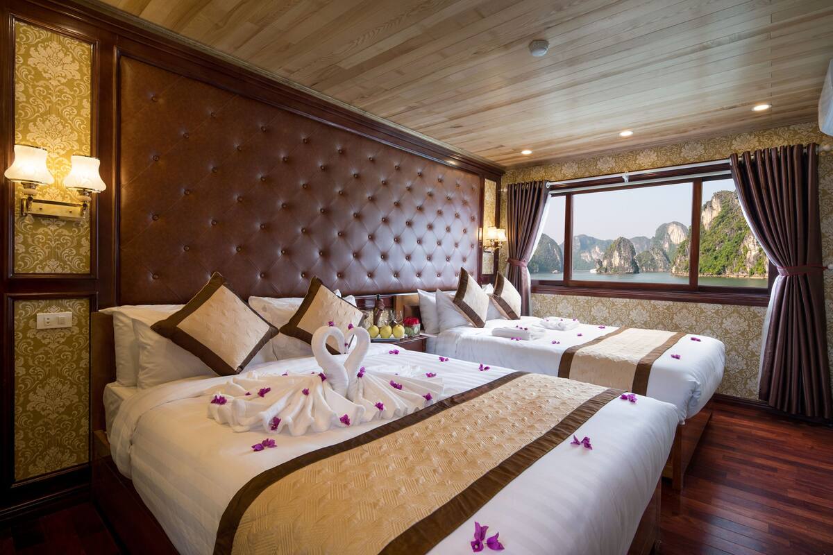 A hotel room with two beds, a large tufted headboard, a view of the sea, and a wooden ceiling.