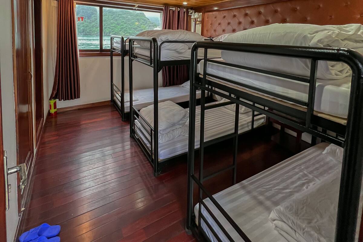 A cabin with bunk beds, wooden flooring, a window with curtains, and an air conditioning unit.