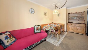 Een gezellige woonkamer met een rode bank, een eettafel met stoelen en een keuken met houten kasten.