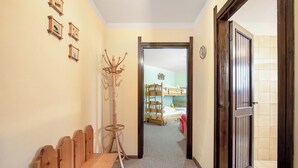 Een gang met een houten bank, een kapstok en een deur die leidt naar een slaapkamer met een bed en een dressoir.