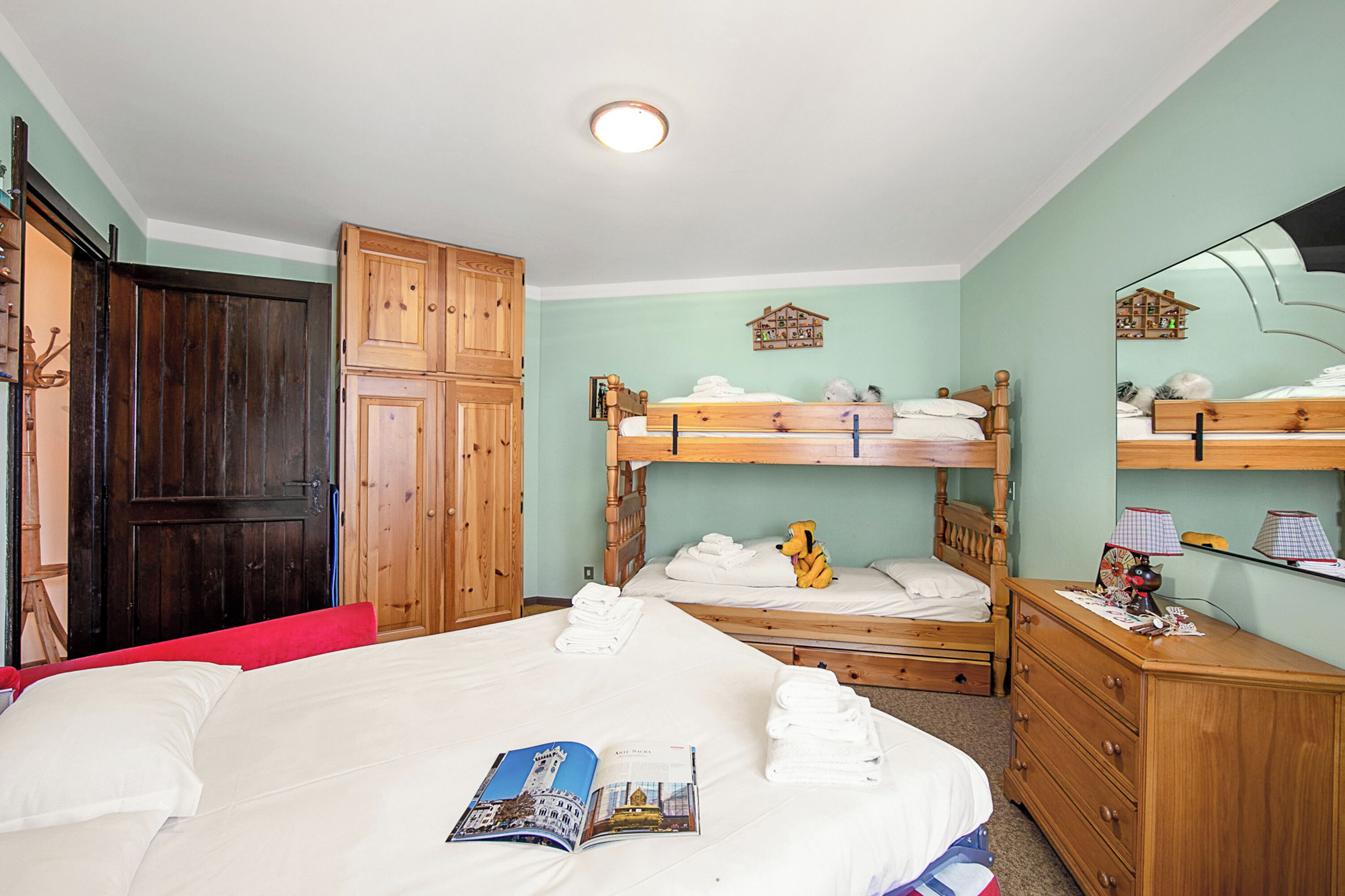 Een slaapkamer met een groot bed, een kleiner stapelbed, houten meubels en een plafondlamp.