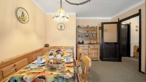 Een eetruimte met een lange tafel gedekt voor een maaltijd, houten stoelen, een kroonluchter en een deur naar een andere kamer.
