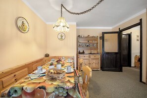 Una sala da pranzo con un lungo tavolo apparecchiato per un pasto, sedie di legno, un lampadario e una porta che conduce in un'altra stanza.