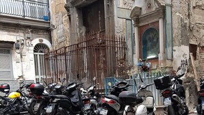 A row of parked motorcycles in front of a building with a weathered facade and a large arched doorway. - Panariello a Portamedina (Napoli)