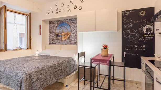 A bedroom with a bed, a small table with a chair, a window, and a chalkboard with writing. - Panariello a Portamedina (Napoli)
