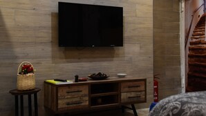A living room with a flat-screen TV mounted on a wooden wall, a wooden cabinet with drawers, a small table with a basket, and a fire extinguisher. - Panariello a Portamedina (Napoli)