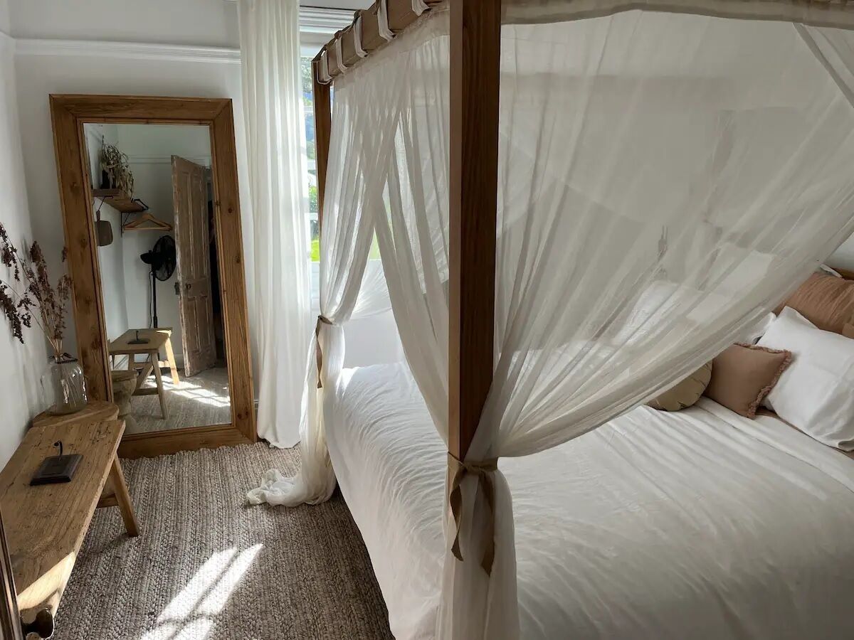 Un dormitorio con una cama con dosel, una mesita de noche de madera y un espejo.