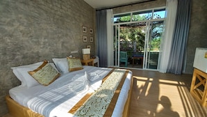 Een slaapkamer met een groot bed, een nachtkastje, een lamp en uitzicht op de natuur via een schuifdeur.