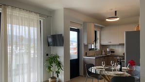 A modern kitchen with a dining area, a TV mounted on the wall, and a potted plant. - MOSSA CITY APARTMENTS (Chania)